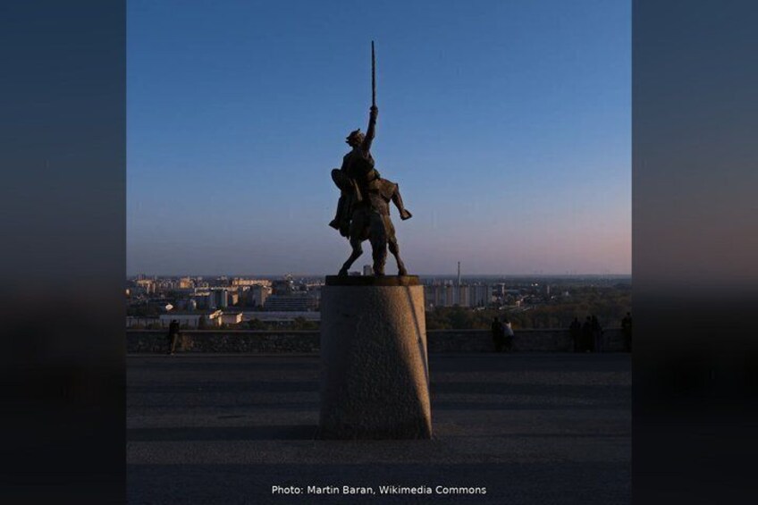 A statue of a warrior on a pedestal with a cityscape in the background. 5