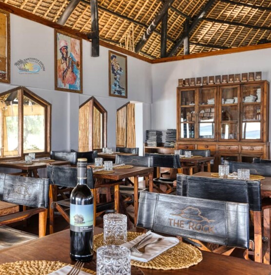 A rustic restaurant interior with wooden tables, woven placemats, and a bottle of wine on one table. 2