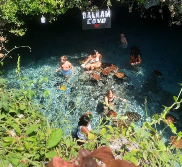 A group of people in a clear water body with a sign reading 'Balaam Cove'. 3