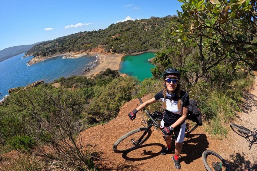 A person on a mountain bike, a coastal landscape with a turquoise sea, and a dirt path. 1