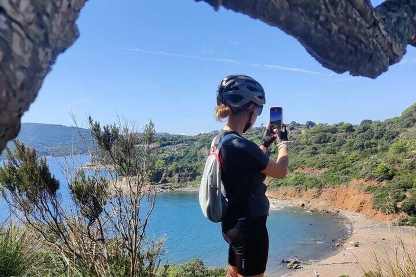 A person taking a photo of a coastal landscape with a clear sky and a rocky outcrop. 4