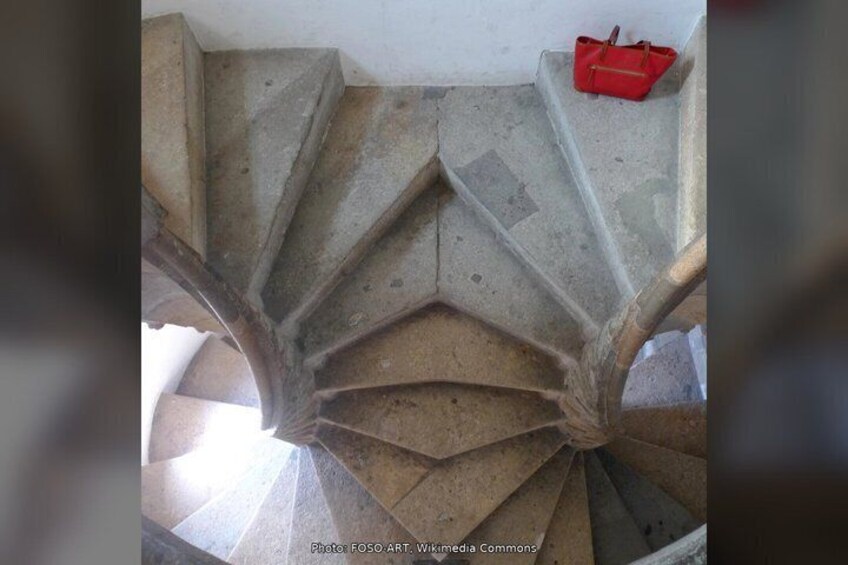 A spiral staircase with a red bag on the landing. 4