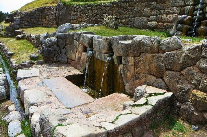 An ancient stone structure with a small waterfall and a stone bench. 5