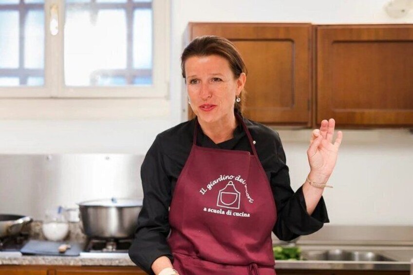 A person in a kitchen wearing a maroon apron with text, standing in front of wooden cabinets and a stove. 1