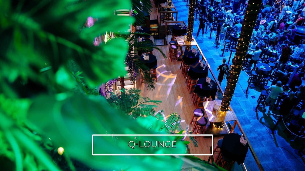 A crowded indoor venue with tables and chairs, surrounded by greenery and decorative lights. 4