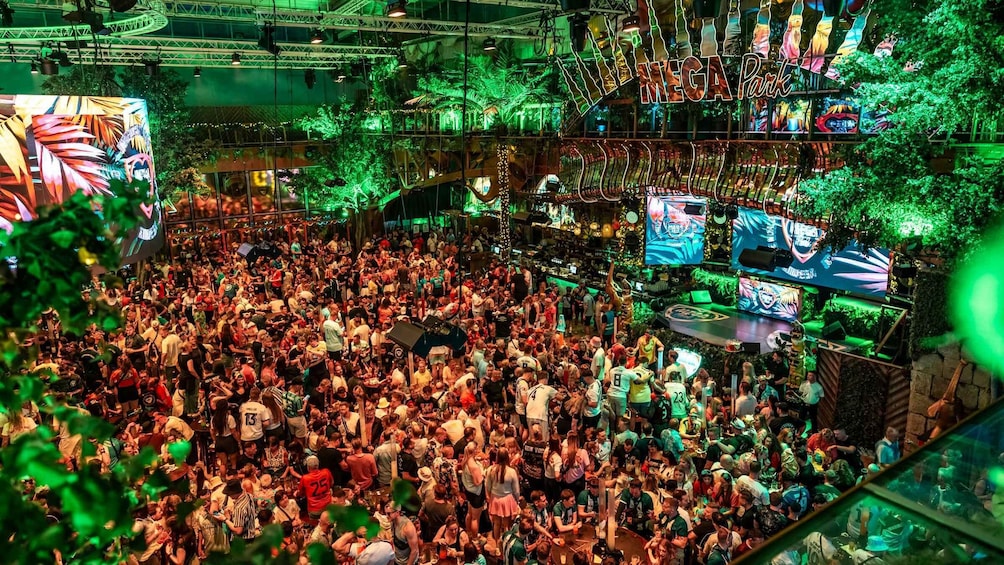 A crowded indoor event with a stage and large screens. 1