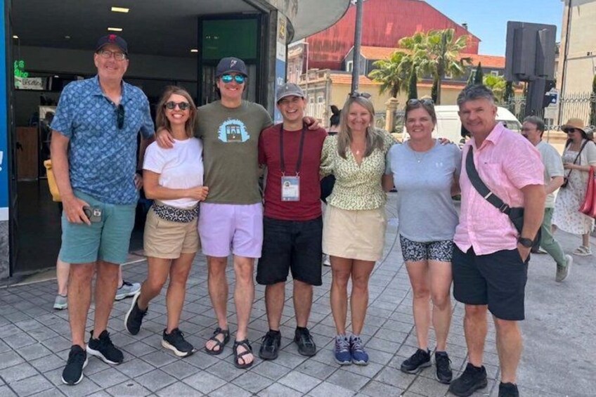 A group of people posing for a photo in an urban setting with a red building and palm trees in the background. 1