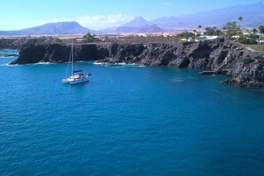 A sailboat on a calm sea with a rocky coastline and mountains in the background. 2