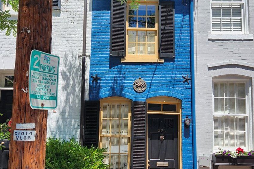 A blue building with a black door and windows, a parking sign, and a tree. 2