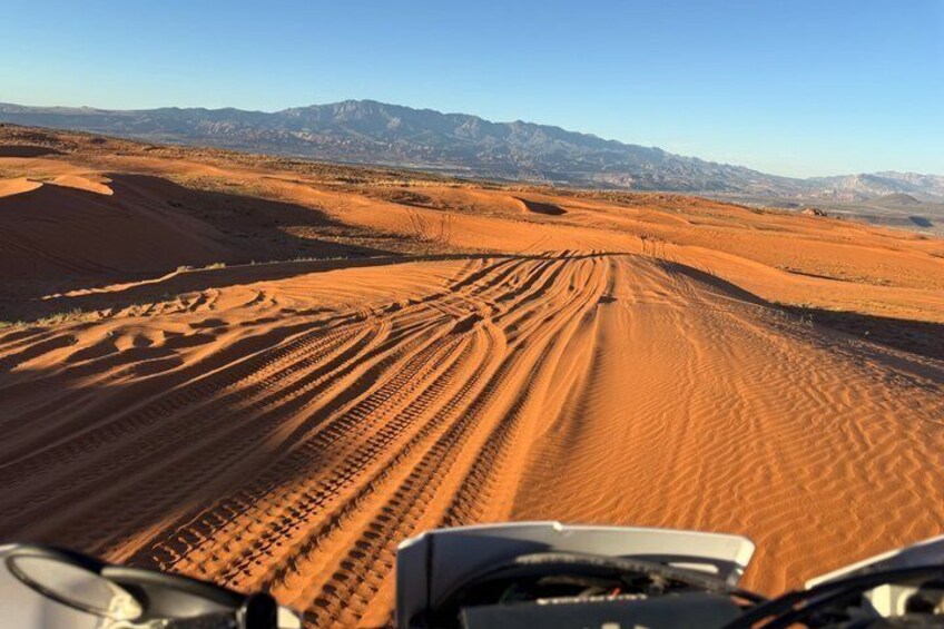 A desert landscape with sand dunes and a vehicle's tracks. 1