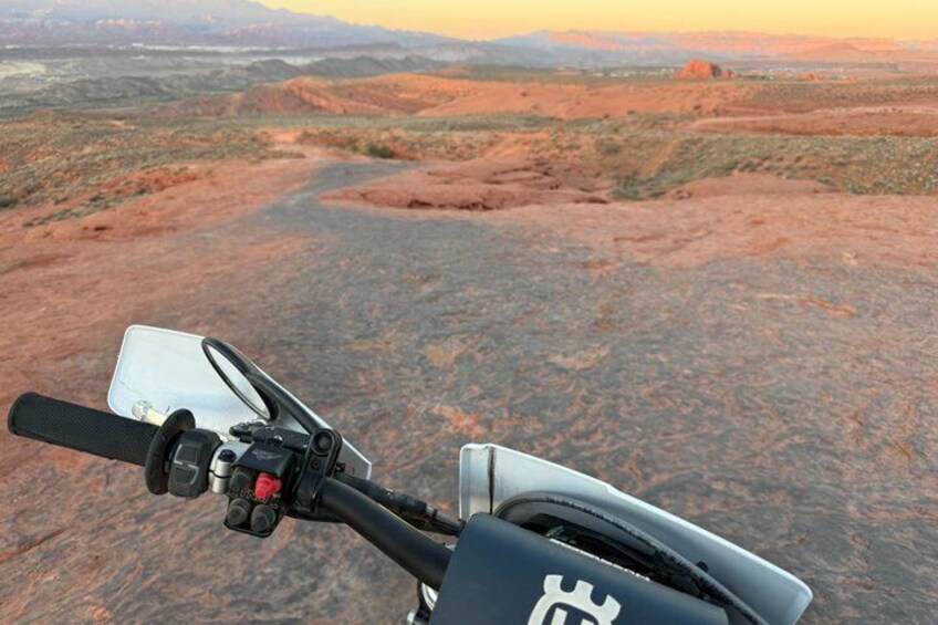 A motorcycle's handlebars and a desert landscape with red rock formations. 3
