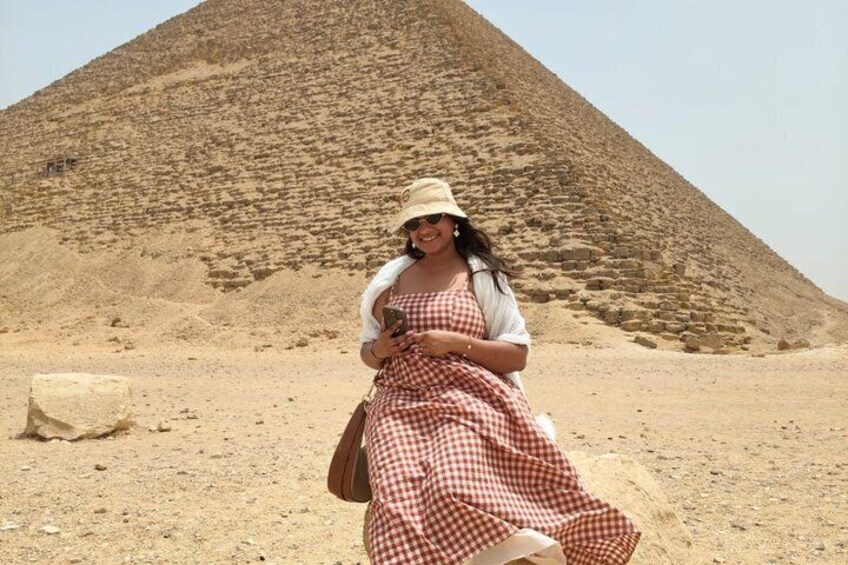 A person in a checkered dress and hat sitting in front of a pyramid. 2