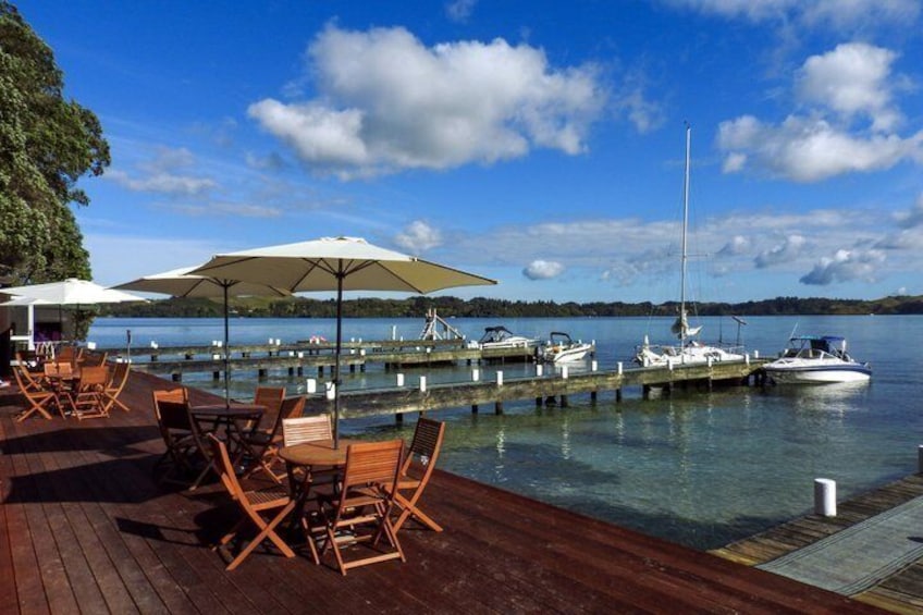 A wooden deck with chairs and umbrellas, a dock with boats, and a calm lake under a blue sky. 3