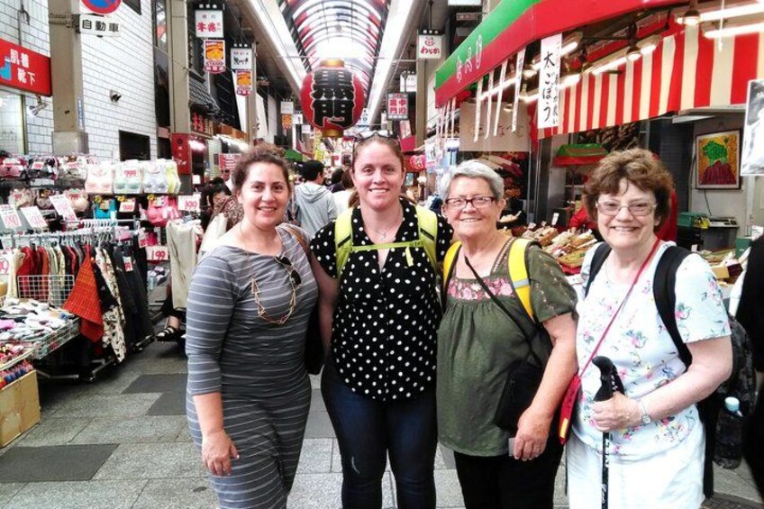 A group of people standing in a market with various stalls and signs in the background. 4