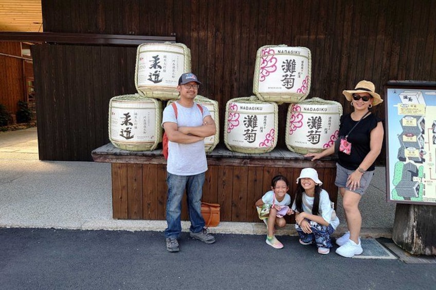 A family posing in front of a display of large sacks with Japanese text, a wooden structure, and a map on the right. 5