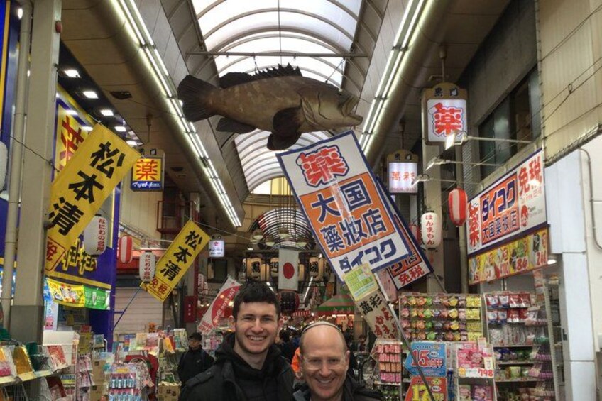 A narrow market aisle with various signs and goods. 2