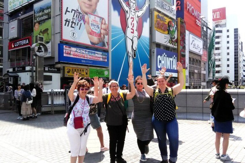 A busy urban street with people standing and raising their hands, surrounded by various commercial billboards and signs. 3