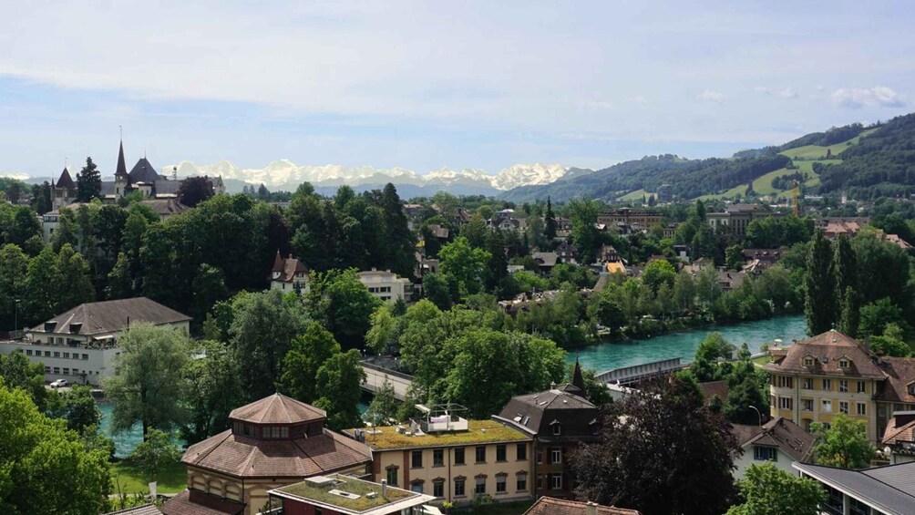 A town with a river, green hills, and snow-capped mountains in the background. 2