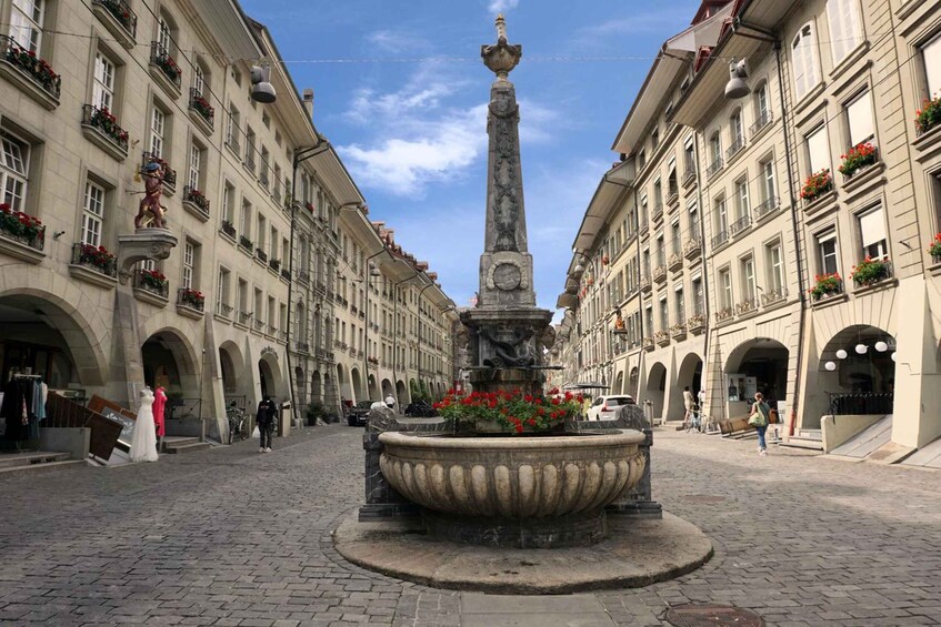 A historic square with a central fountain, flanked by classical architecture and pedestrians. 4