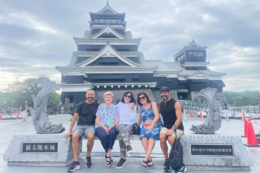 A group of people sitting on a bench in front of a traditional Japanese building with a pagoda-style roof. 1