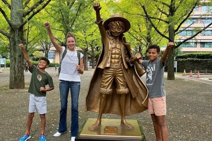 A bronze statue of a character with raised arms, surrounded by trees and a paved area. 4