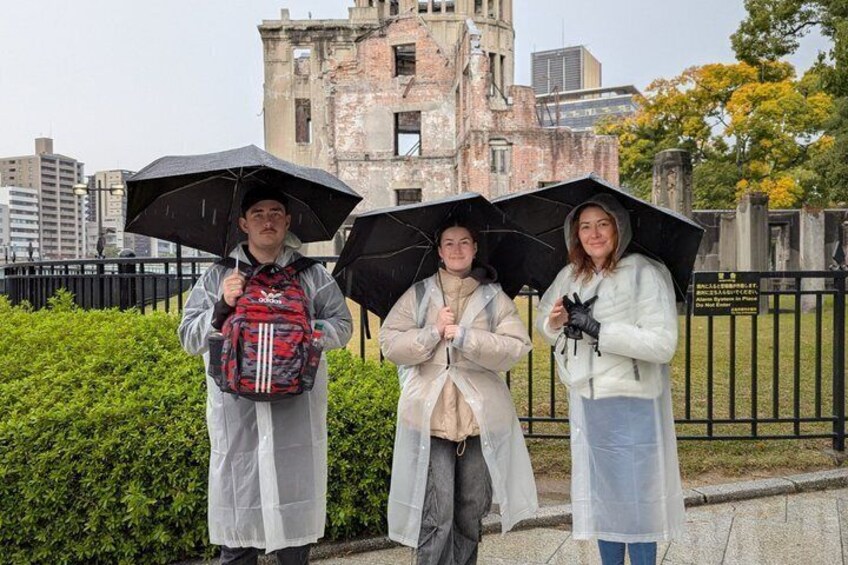 Three people holding umbrellas, standing in front of a historic building with a fence and greenery in the background. 5