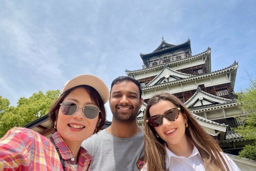 Three people in front of a traditional Japanese castle with multiple tiers and a curved roof. 2