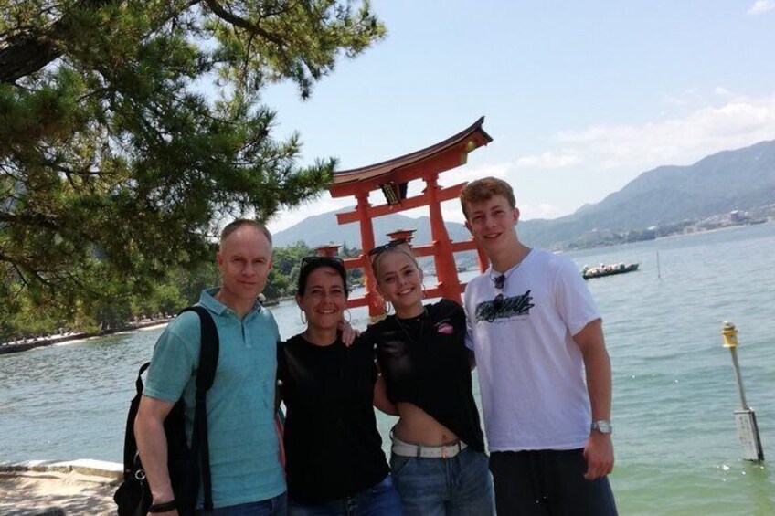 A group of people standing in front of a red torii gate by a lake with mountains in the background. 1