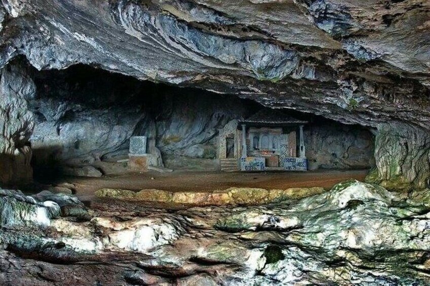 A cave with a small structure inside, surrounded by rocky terrain. 3
