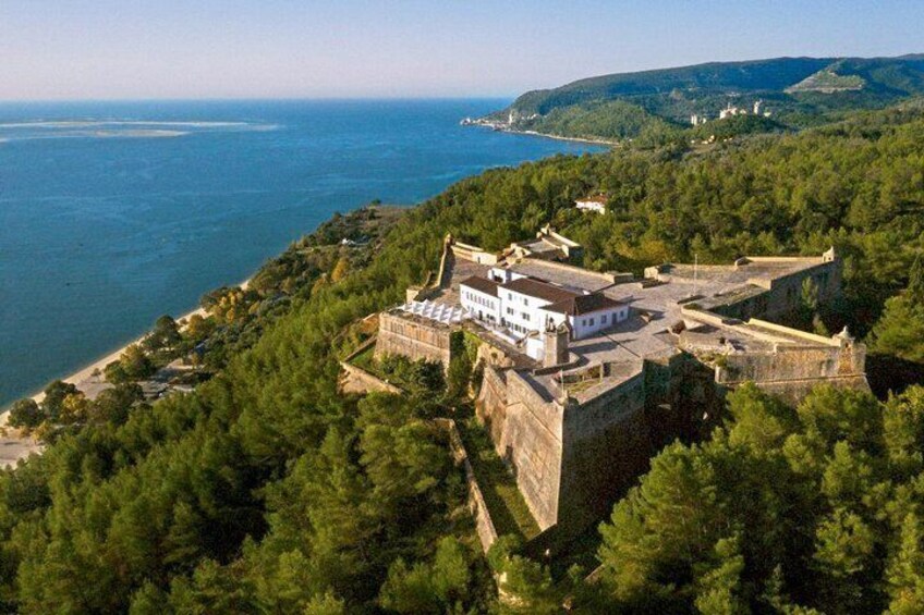A coastal fortification with a white building, surrounded by dense forest and overlooking the sea. 5