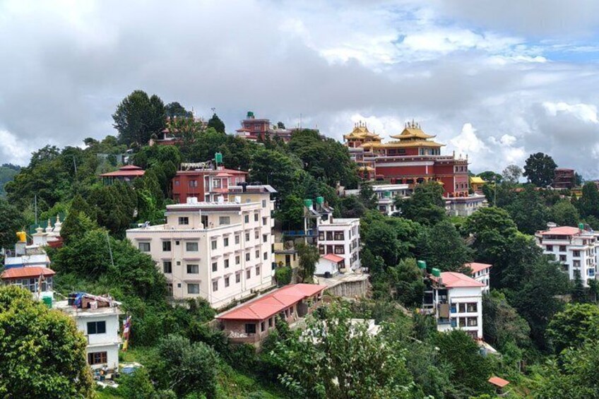 A mountainous town with buildings, trees, and a temple with golden roofs. 1