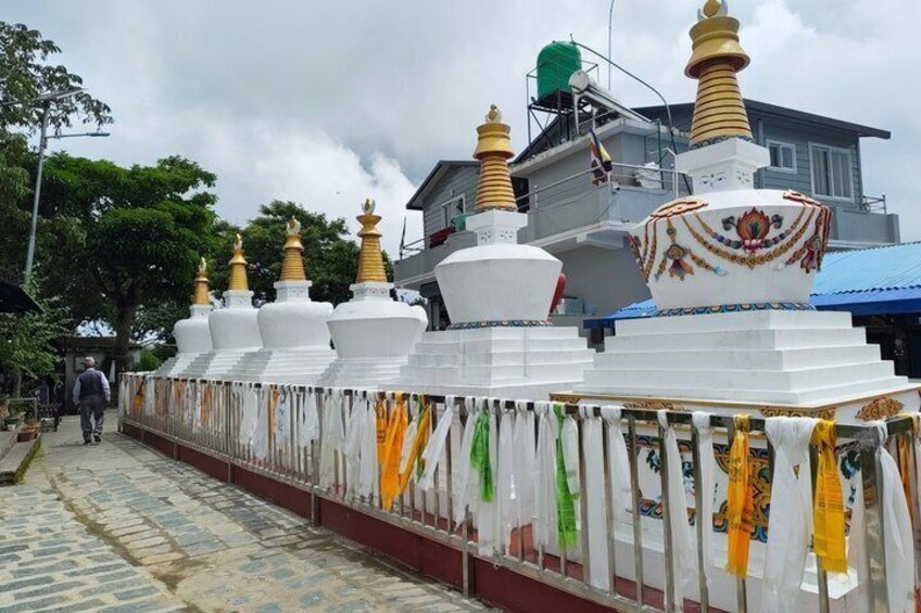 A row of white stupas with golden tops, adorned with colorful prayer flags, and a building in the background. 4