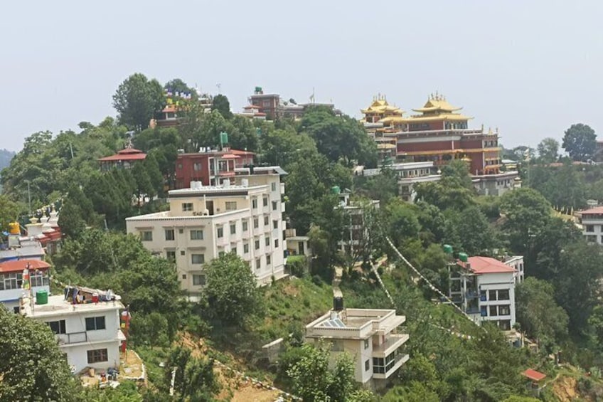 A hillside with buildings, including a multi-story structure with a red roof and a traditional building with golden roofs. 1