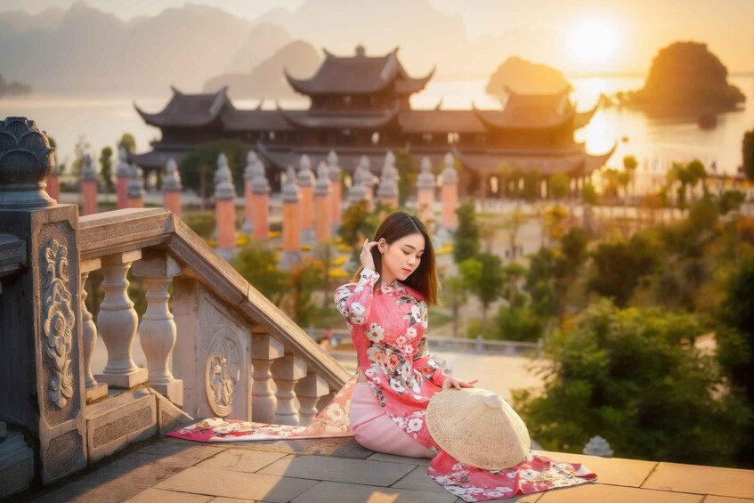 A person in traditional attire sitting on a staircase with a view of traditional architecture and a body of water in the background. 3