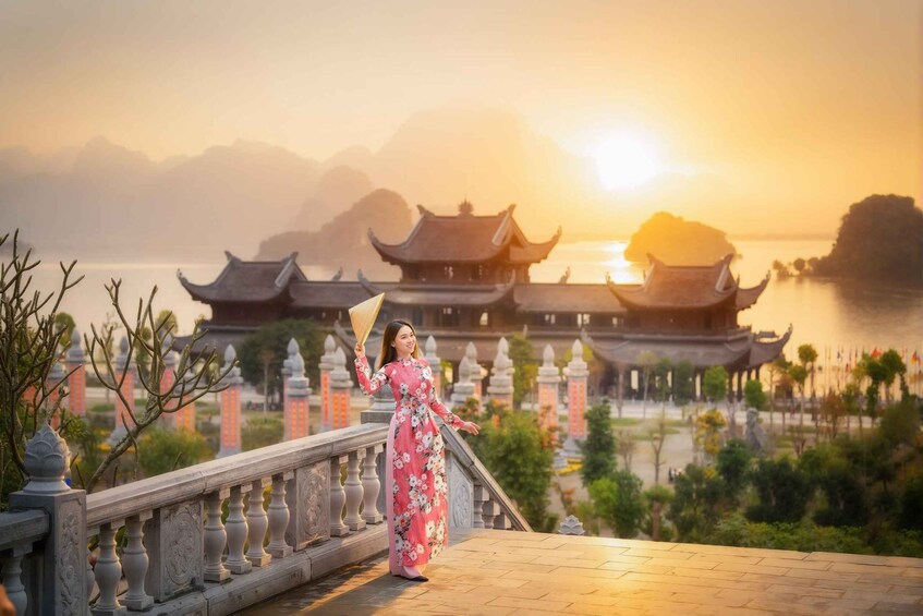 A person in a pink floral dress standing on a bridge with traditional architecture in the background. 5
