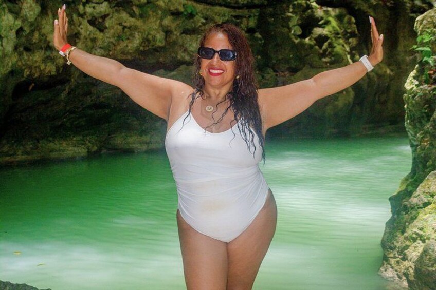 A person in a white swimsuit standing in a body of water with arms raised, surrounded by rocky terrain. 5