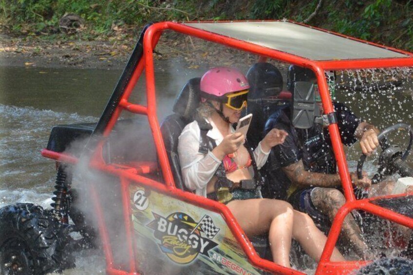 A red off-road vehicle with two people, one wearing a helmet, on a river. 1