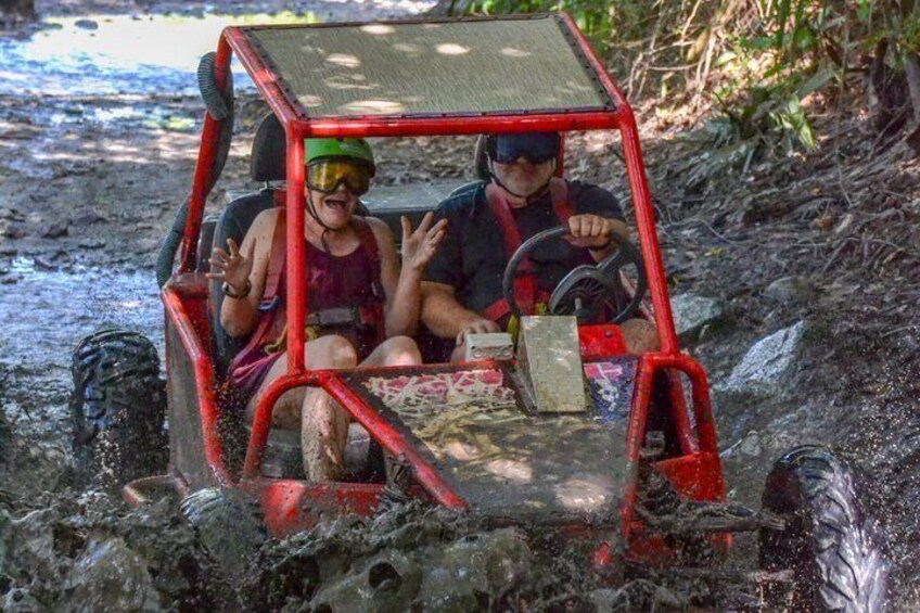 Two people in a red off-road vehicle navigating through a muddy terrain. 2
