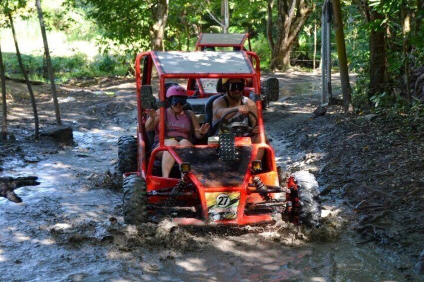 A red off-road vehicle navigating a muddy path in a forested area. 3