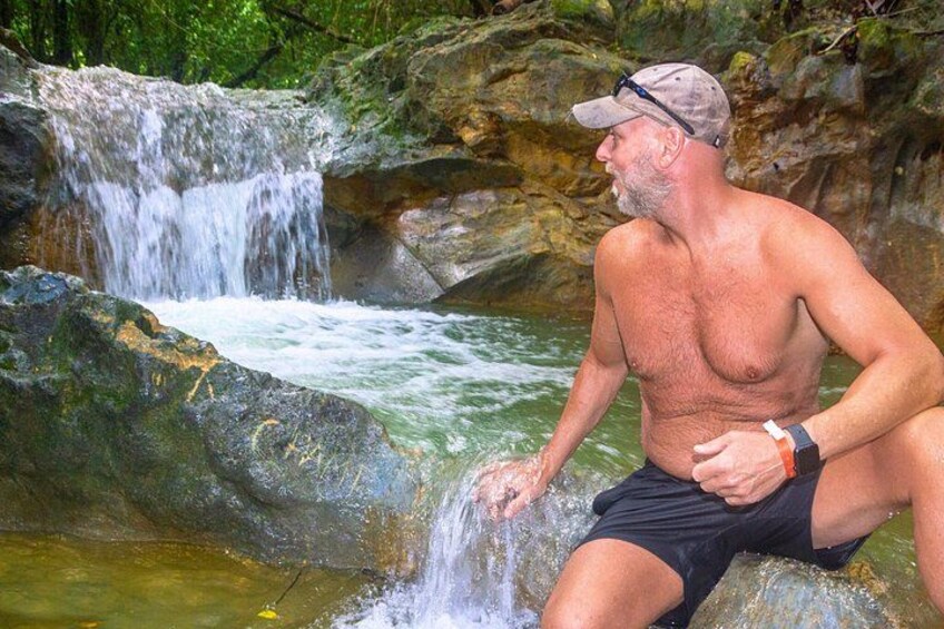 A man sitting by a waterfall in a forested area. 3