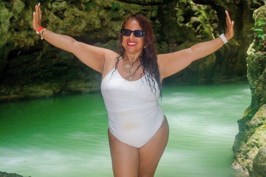 A person in a white swimsuit standing in a body of water with arms raised, surrounded by rocky terrain. 5