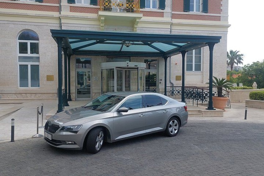 A silver car parked in front of a building with a covered entrance and a glass door. 2