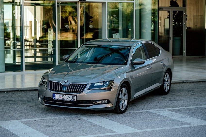 A silver car parked in front of a building with large windows. 1
