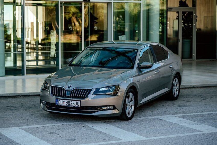 A silver car parked in front of a modern building with large glass windows. 1