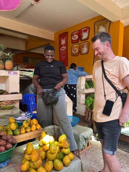 A market stall with various fruits and vegetables, a person holding a plastic bag, and another person standing nearby. 2