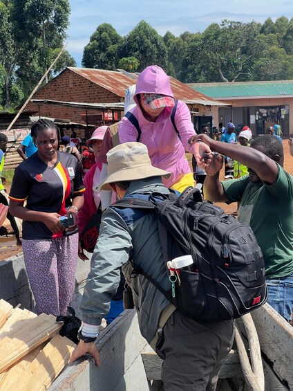 A group of people outdoors, some wearing hats and carrying backpacks, with a brick building and trees in the background. 5