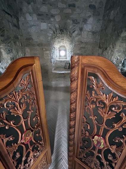 An ornate wooden door with intricate carvings, leading to a stone wall with a small window. 5