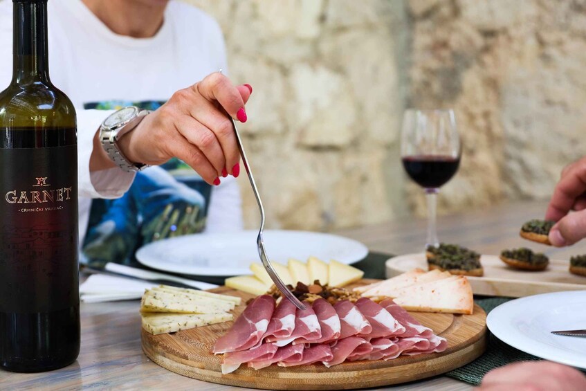 A person cutting prosciutto on a wooden board with cheese and other items on a table. 5