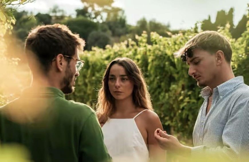 Three people standing outdoors with greenery in the background. 4