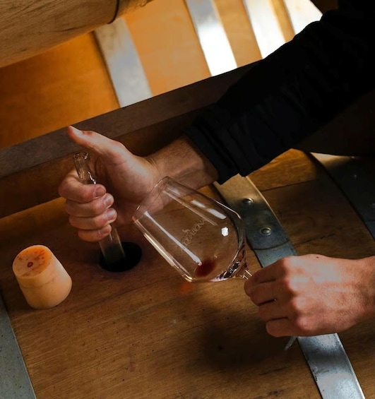 A person pouring a liquid from a bottle into a glass on a wooden surface. 3